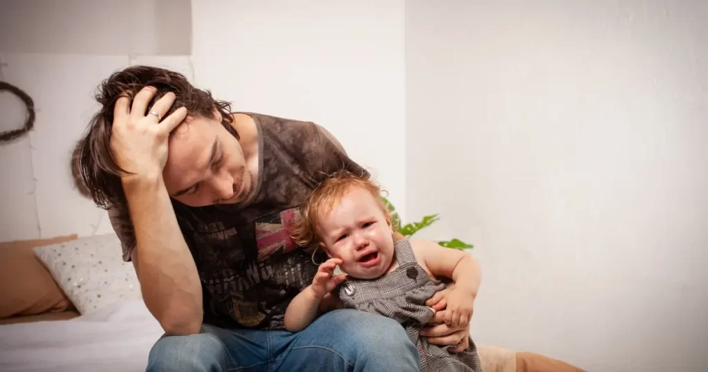 泣き止まない赤ちゃんを手に頭を抱えるパパ